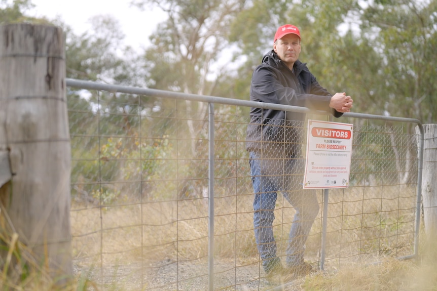 Man standing behind a metal fence with a sign about farm biosecurity.