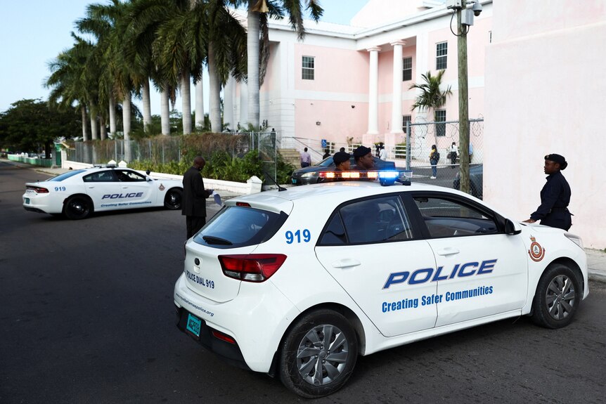 A police car parked outside a pink columned building