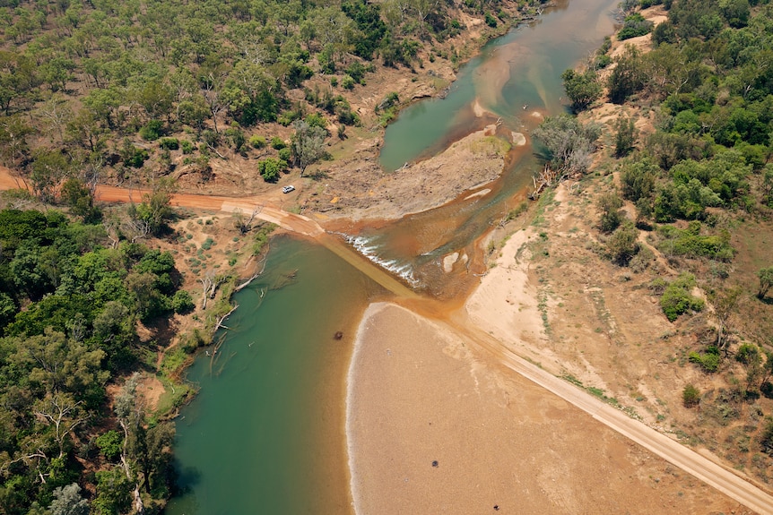 Aerial view of a river with a dirt road through the middle and cleared land in the foreground.