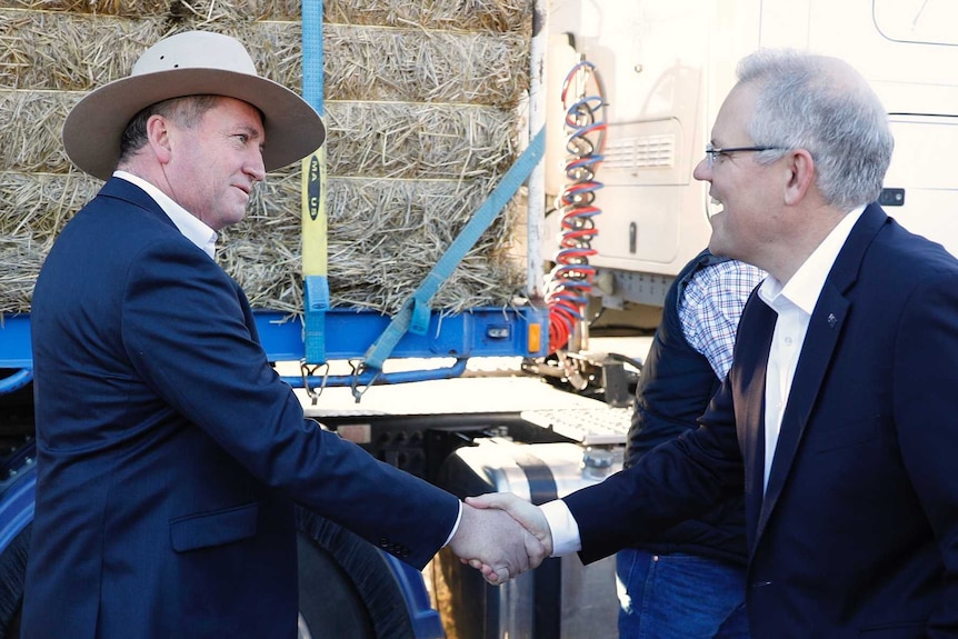 Mr Joyce, wearing an Akubra, and Mr Morrison shake hands in front of a semi-trailer with hay on it