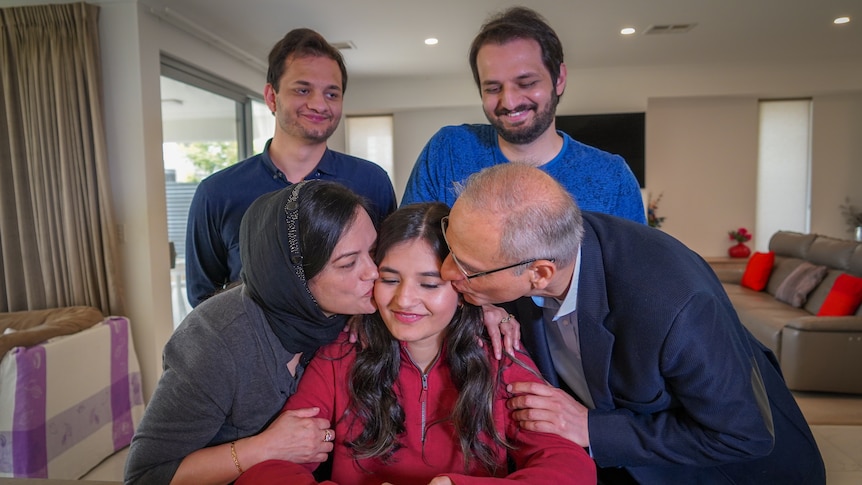 A man and a woman kissing a younger woman looking at a laptop while two other men stand behind