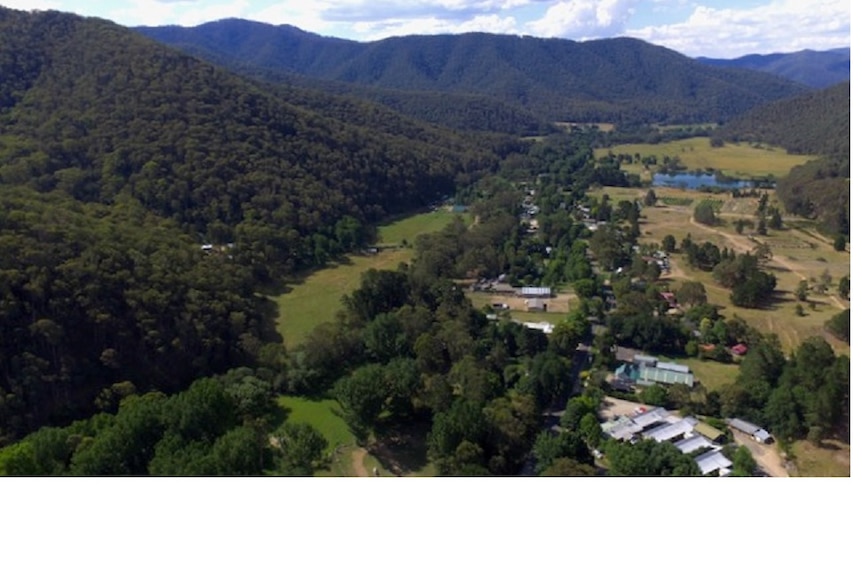 A drone picture looking down on a town in an alpine valley, with a dredge hole in the background. 