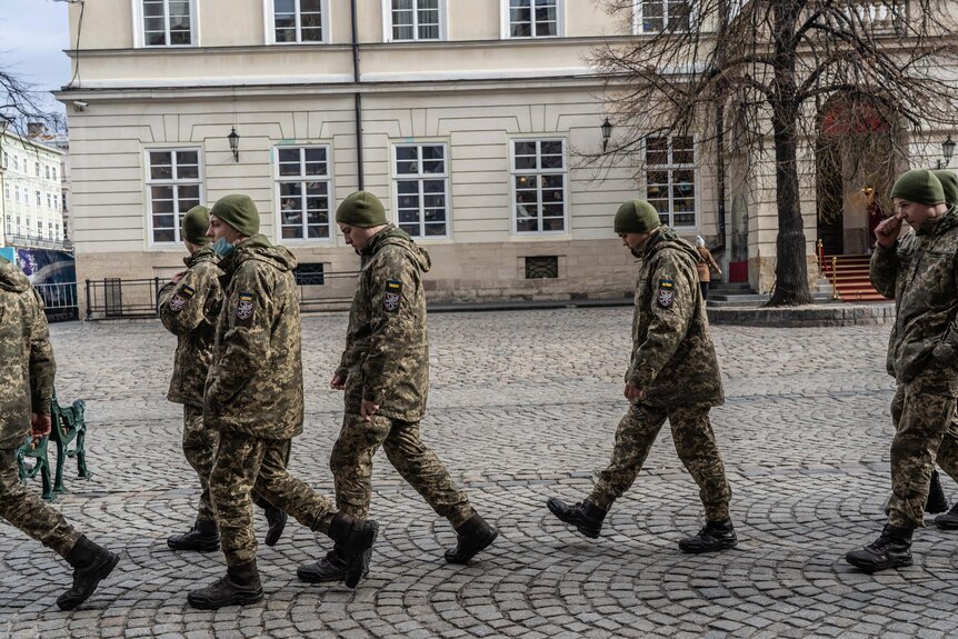 Men wearing camouflage uniforms stroll down a street.