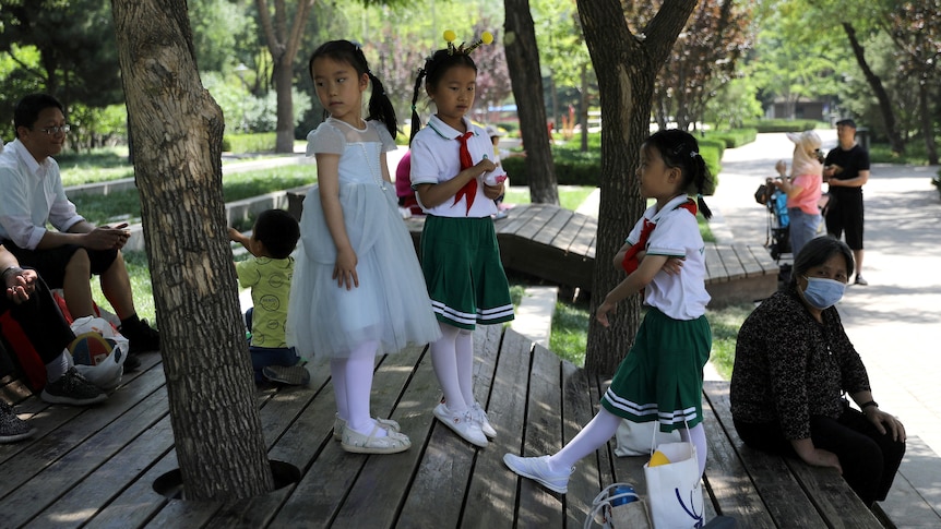 Children play next to adults at a park in Beijing, China