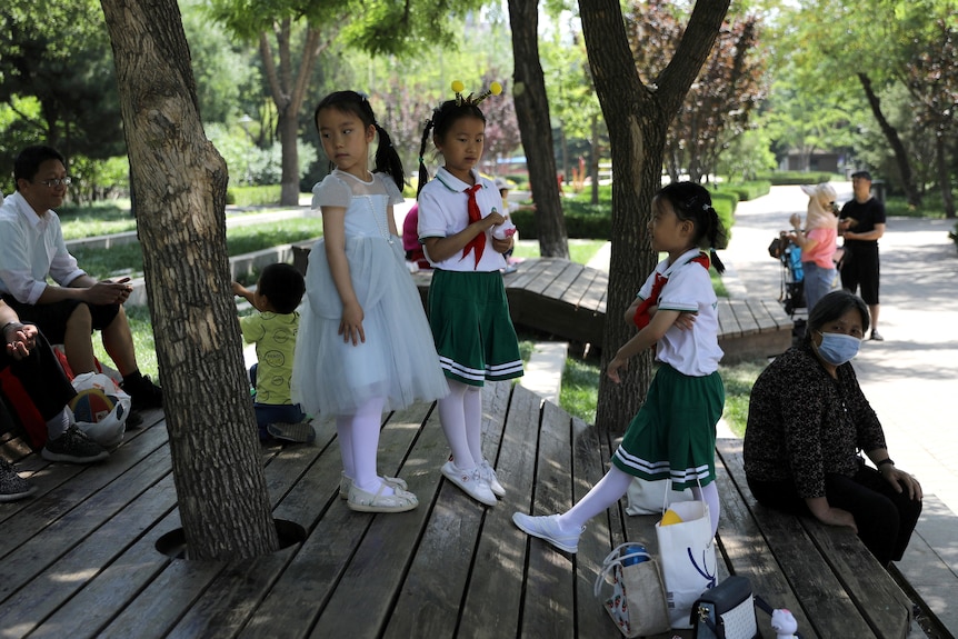 Children in white and green clothes play next to adults at a park in Beijing, China.