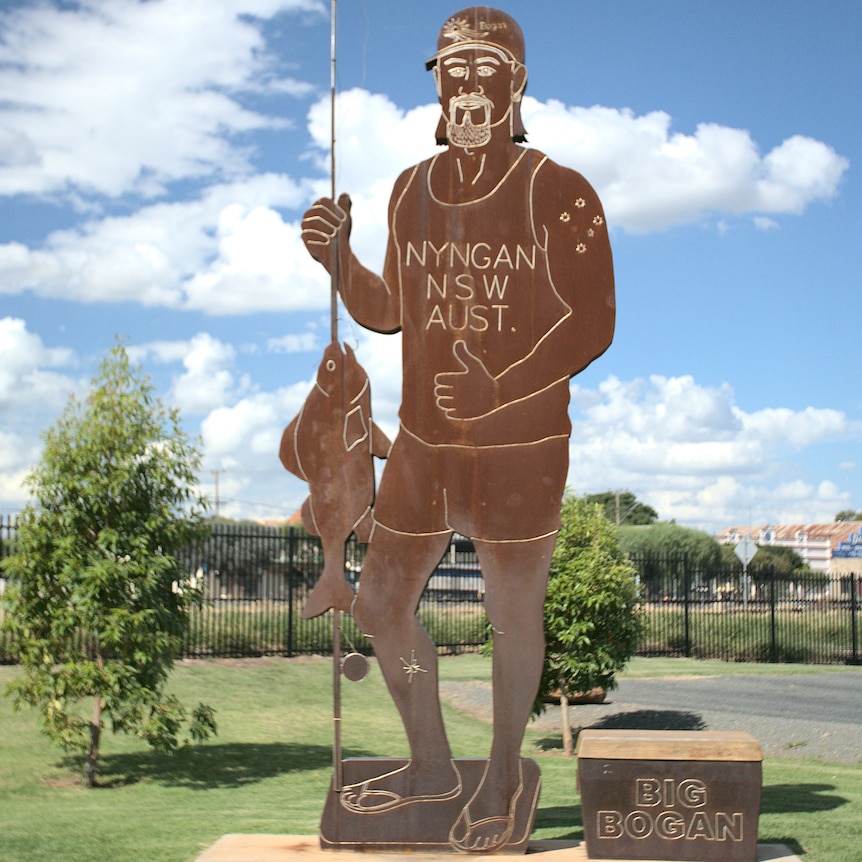 A big metal statue of a man in a singlet and thongs, holding up a fish.