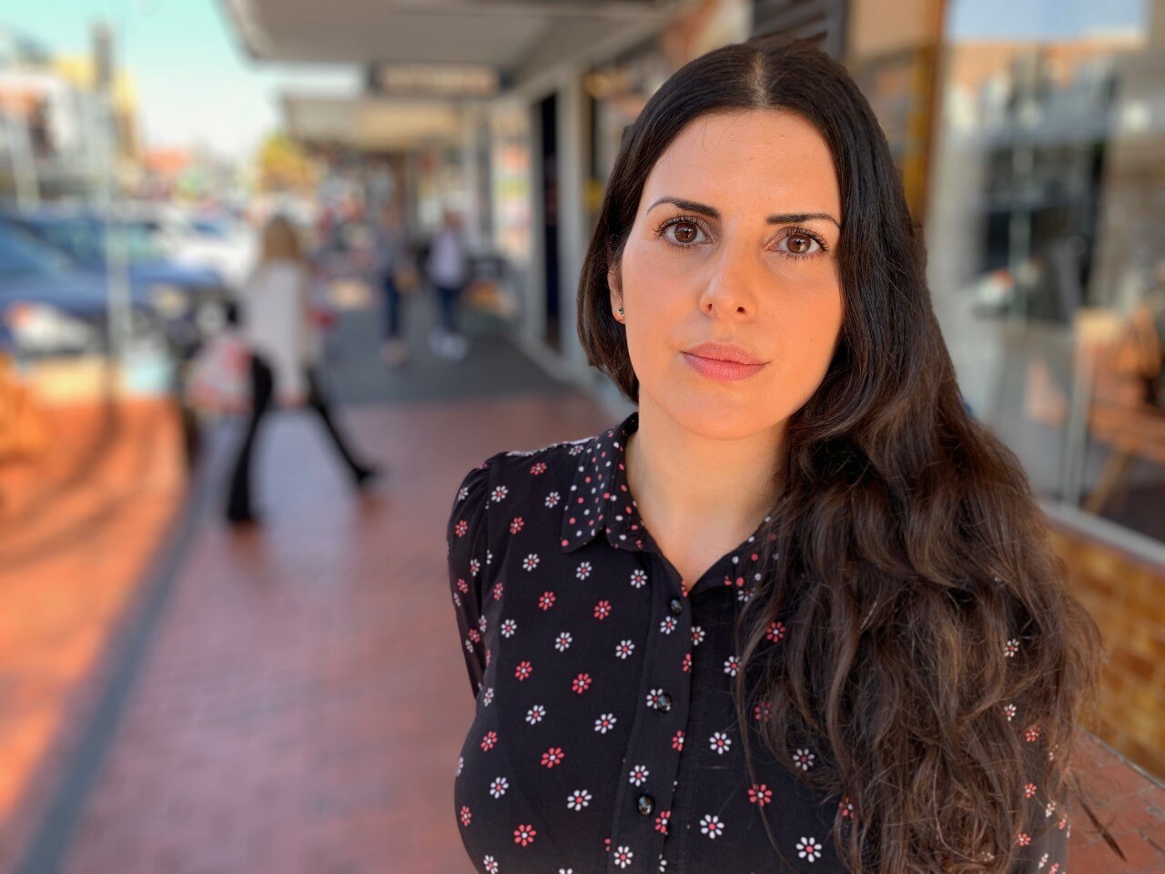 A young woman with long dark hair standing out on a footpath