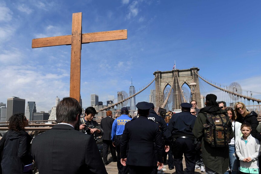 Vitaly Kuzmin holds a cross as he leads the Way of the Cross procession across the Brooklyn Bridge with NYPD officers