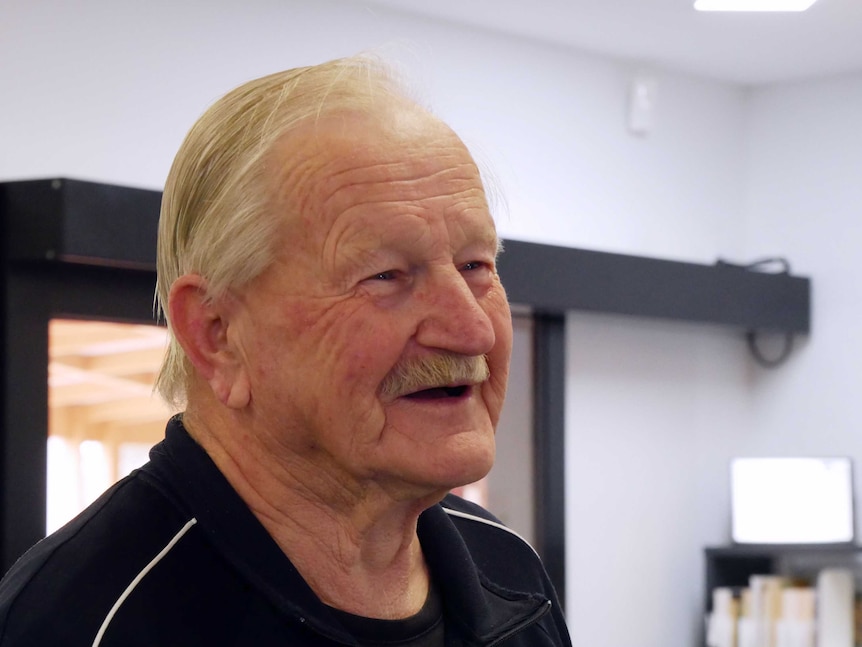 An older man with blonde/grey hair looking to the right, smiling kindly.