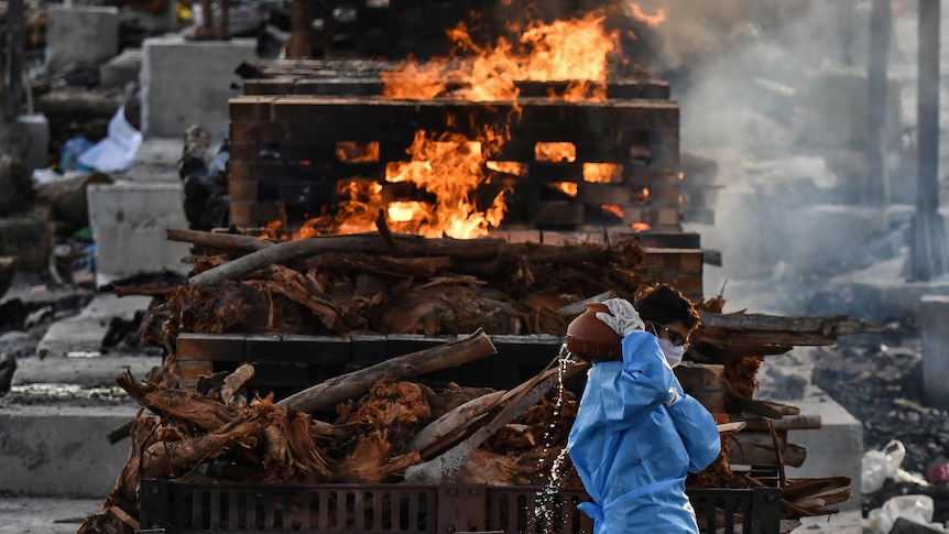 The son of a man who died of COVID-19 walks past piles of burning wood before his father's cremation.