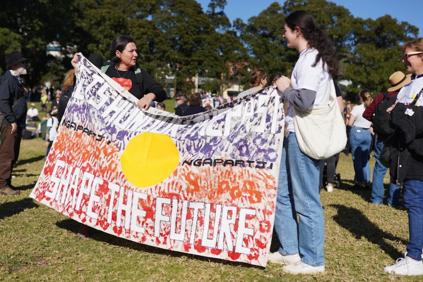 Two people hold a Aboriginal flag Surry Hills' Prince Alfred Park at the Come Together For Yes rally