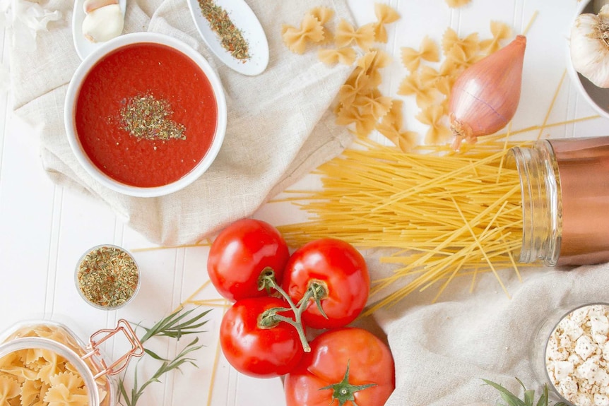 Flat lay photo showing pasta, tomato sauce, onions and spices, showing time saving pantry staples.