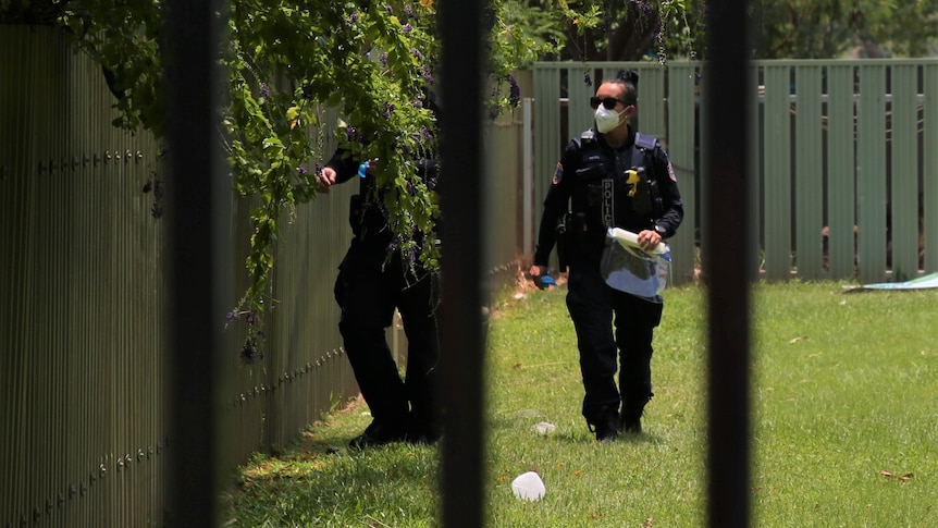 Police walk through a lawn at a house block on the Victoria Highway.