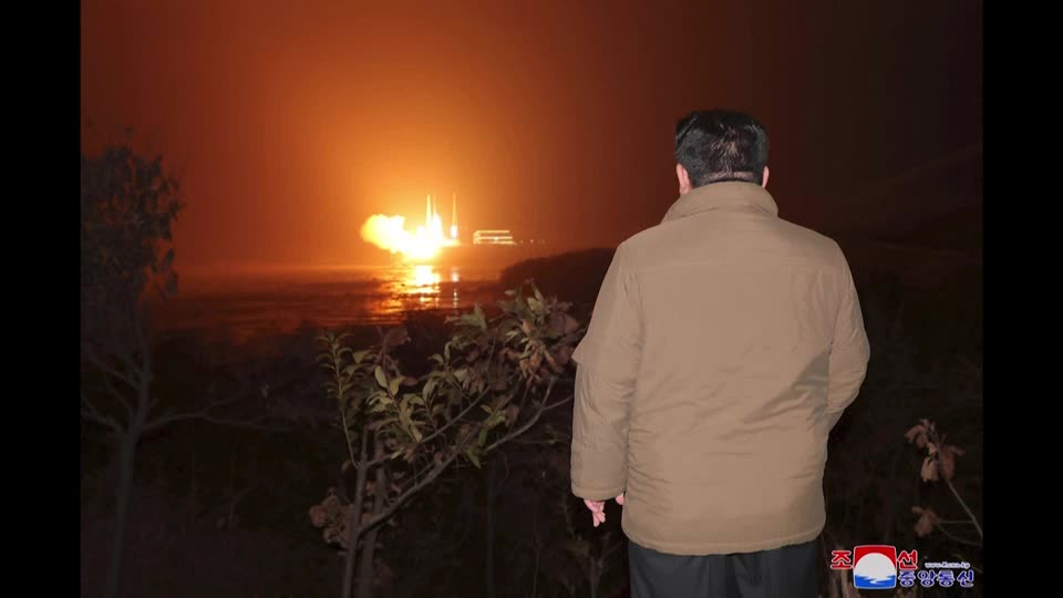 The back of Kim Jong Un in front of a rocket launch. 