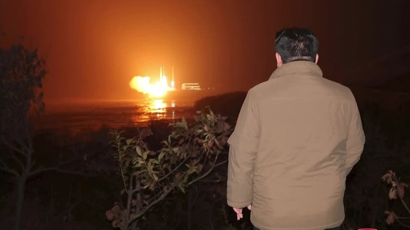 The back of Kim Jong Un in front of a rocket launch. 