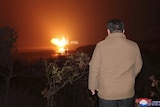 The back of Kim Jong Un in front of a rocket launch. 