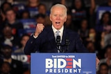 Joe Biden raises fist in the air as he stands at a podium speaking to supporters