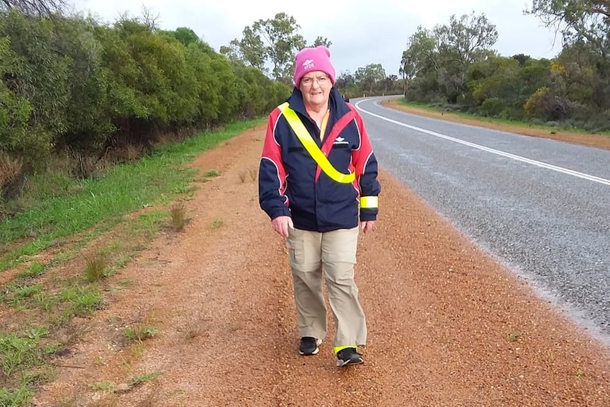 A woman walks towards the camera wearing a beanie and jumper next to a road