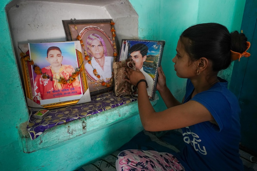 A little Indian girl polishes photos of a man and a woman propped up on a shelf 