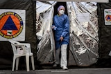 A woman wearing hospital scrubs and a face mask walks through the opening of a silvery tent.