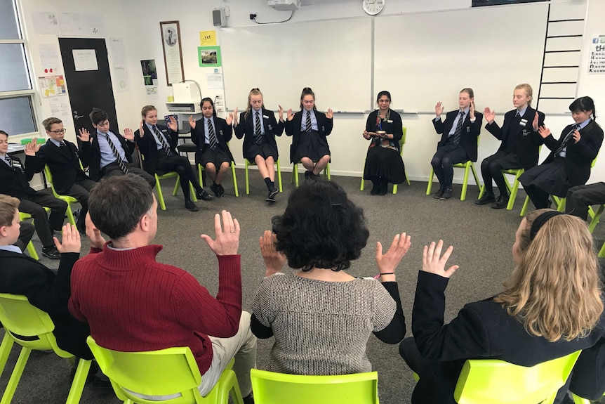 Students sit in a circle, raising their arms as they listen to tibetan bells