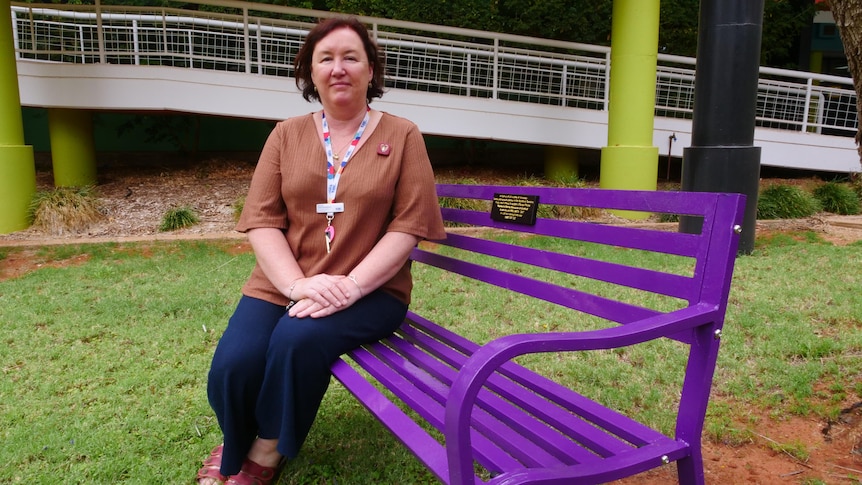 A woman sits on a bright purple park bench in a university courtyard.