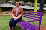 A woman sits on a bright purple park bench in a university courtyard.