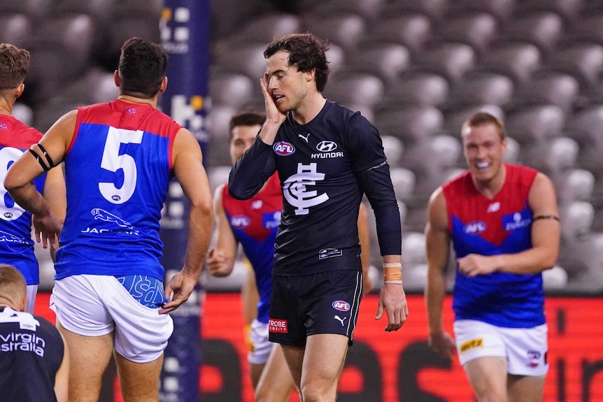 Cameron Polson holds his hand to his face in disappointment as Melbourne players celebrate