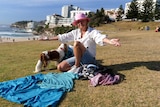 A woman with a small dog gestures over a pile of clothing and towels