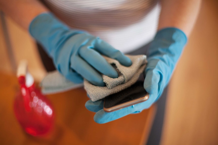 A person wipes down their mobile phone with a cloth