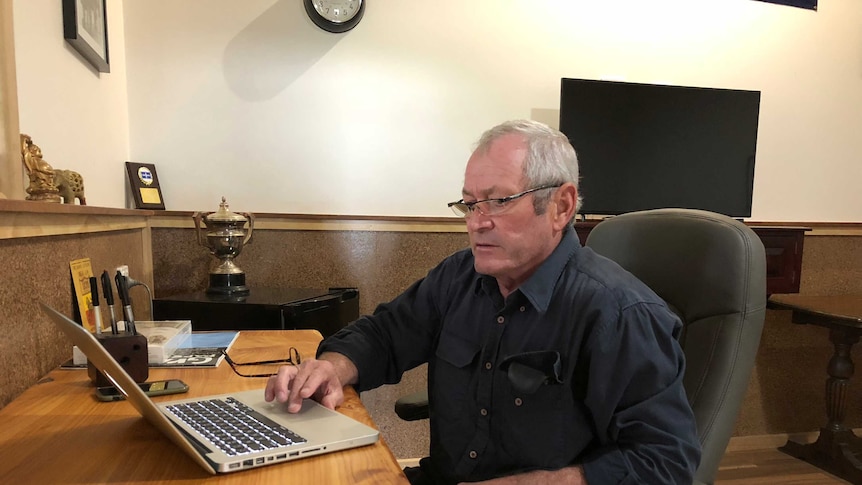 A middle-aged man wearing spectacles sits in a home office working on a laptop