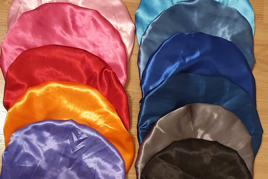 Multiple silk and satin bonnets lined on a table.