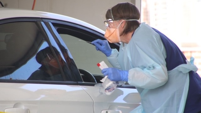 Woman wearing PPE leaning into car at drive-thru coronavirus testing clinic, Burnie, Tasmania, April 2020.