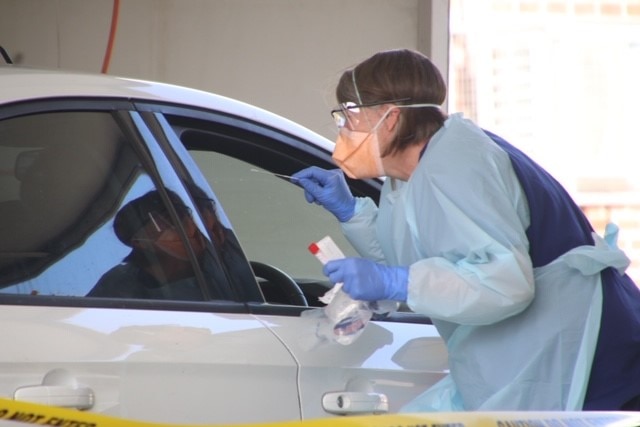 Woman wearing PPE leaning into car at drive-thru coronavirus testing clinic, Burnie, Tasmania, April 2020.