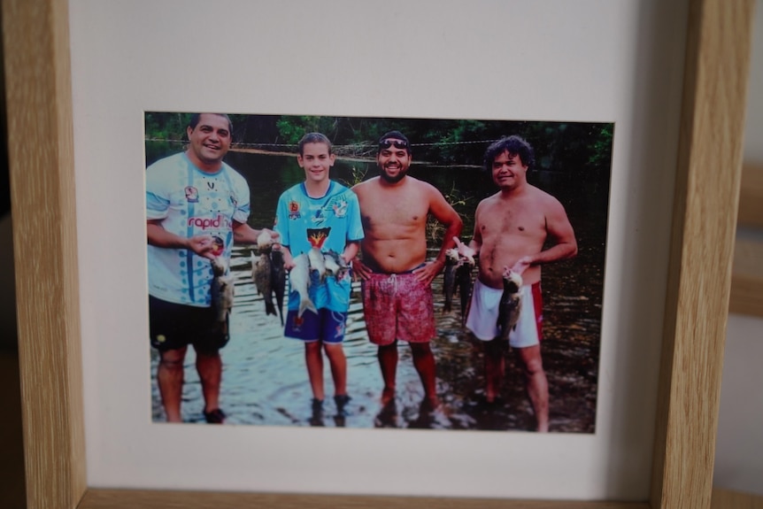 Three men are standing with Jai holding fishes in the middle of a lake