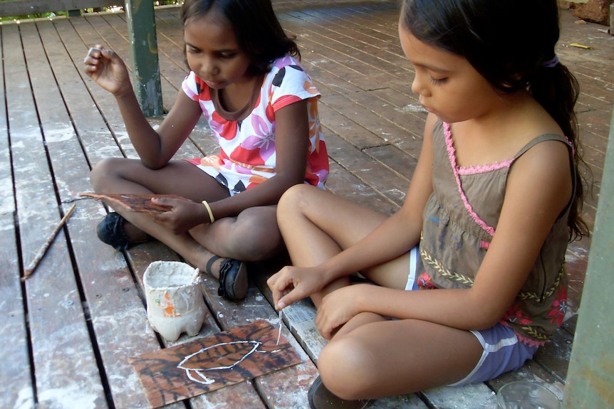 Two young Indigenous girls work on a painting.