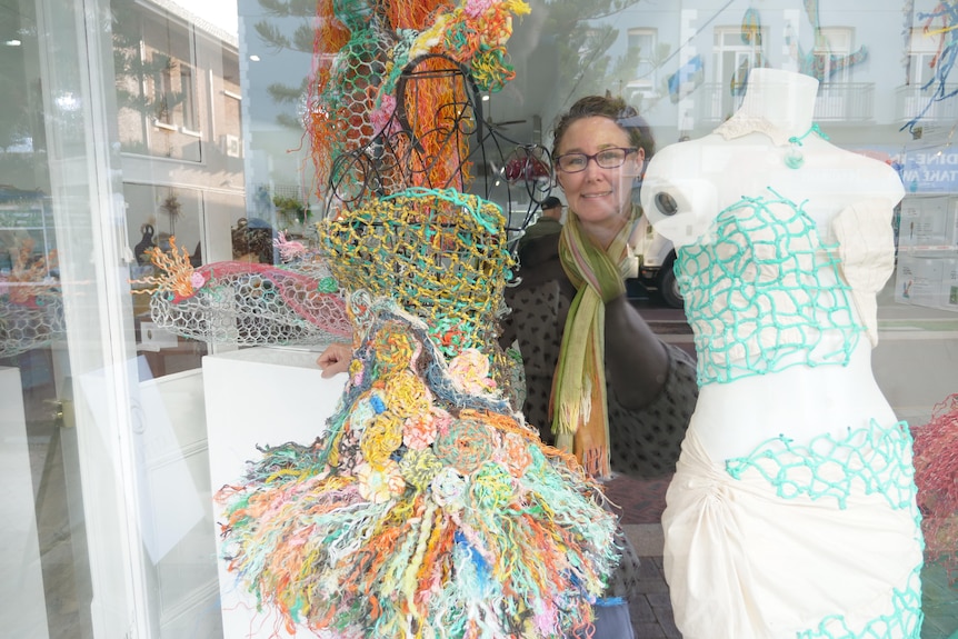 Smiling woman standing behind shop window with a costume made from rope and net