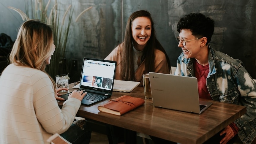 Friends laughing around a work desk in a story about the line between being friendly and friends with your boss.