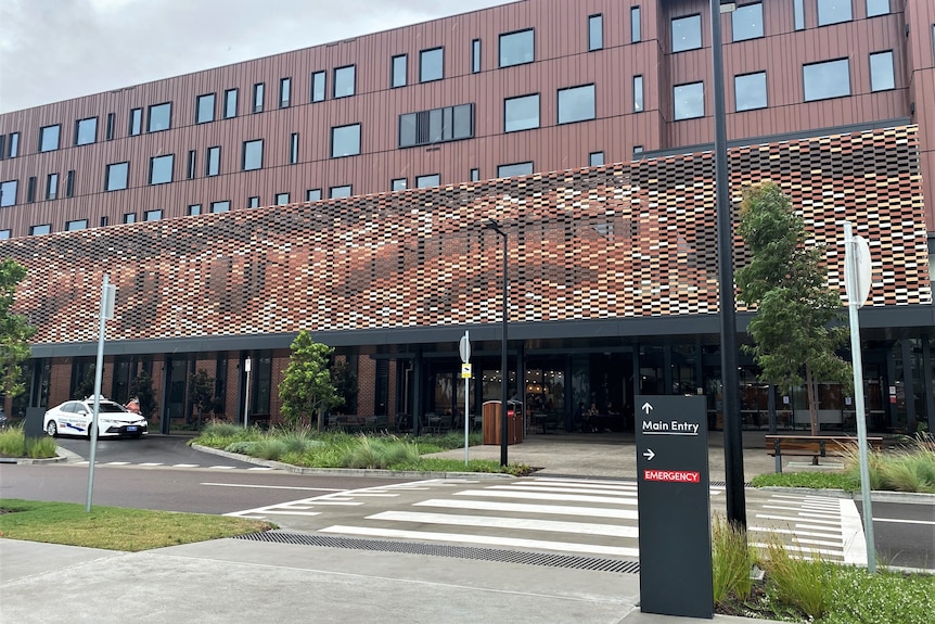 A black sign saying 'main entry' in front of a large rust-coloured hospital building.