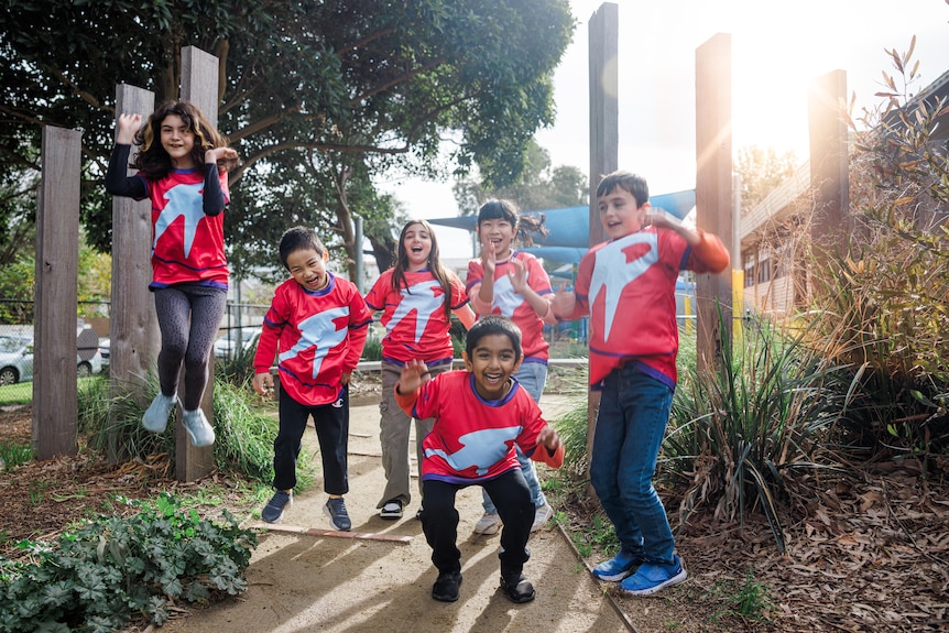 A group of children in matching shirts standing on a pathway, gardens are visible on either side