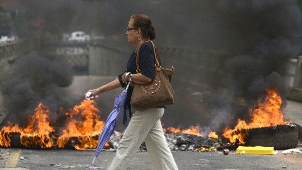 A woman walks by a burning barricade in Caracas