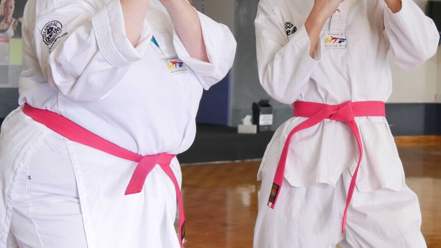 Two women in taekwondo uniforms stand in self-defence pose.
