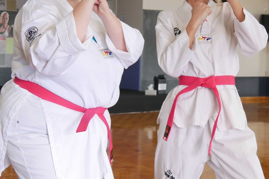 Two women in taekwondo uniforms stand in self-defence pose.