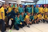 The Australian men's hockey team, the Kookaburras, stand and crouch together for a photo at Perth Airport wearing team uniform.
