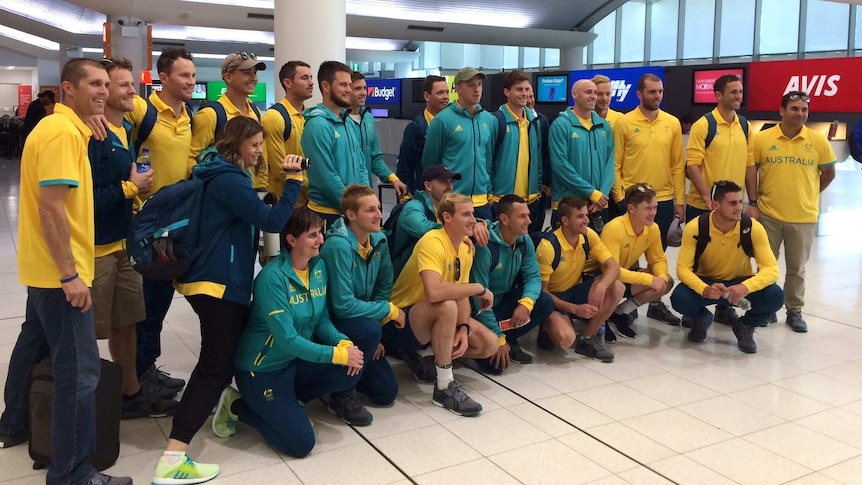 The Australian men's hockey team, the Kookaburras, stand and crouch together for a photo at Perth Airport wearing team uniform.