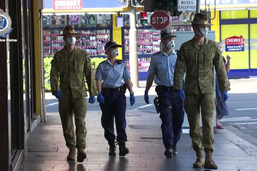 Two soldiers in military uniforms and two police officers walk along a street. 
