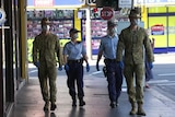 Two soldiers in military uniforms and two police officers walk along a street. 