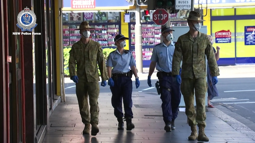 Two soldiers in military uniforms and two police officers walk along a street. 