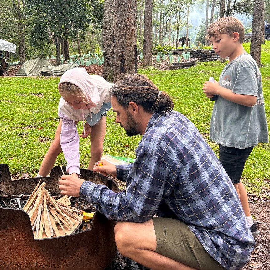 A man and two kids build a fire at a campground.