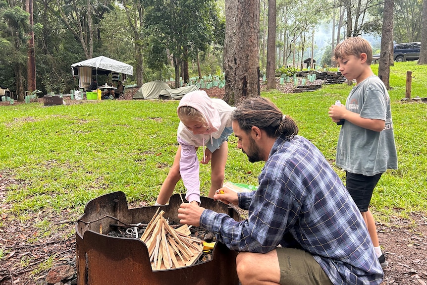 A man and two kids build a fire at a campground.